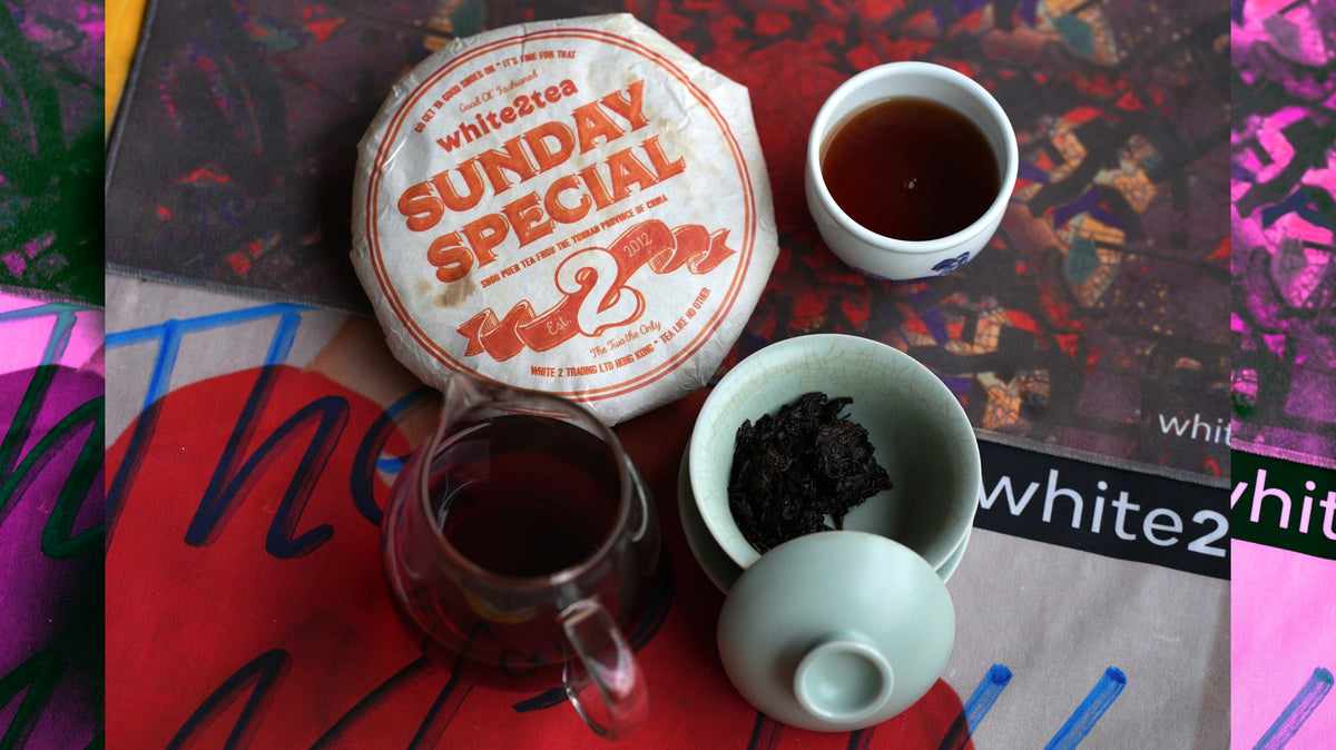 white2tea sunday special ripe puerh tea cake on a tea towel with gongfucha equipment (gaiwan, teacup, and sharing pitcher)