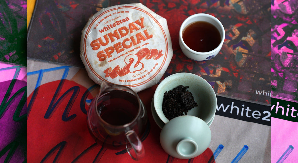 white2tea sunday special ripe puerh tea cake on a tea towel with gongfucha equipment (gaiwan, teacup, and sharing pitcher)
